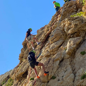 Two men abseiling down a rock face in Malta, secured with ropes and harnesses.