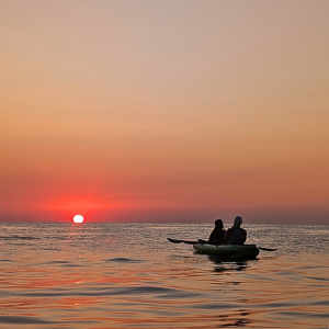 Couple watching the sunrise from a kayak in Malta on calm morning water.
