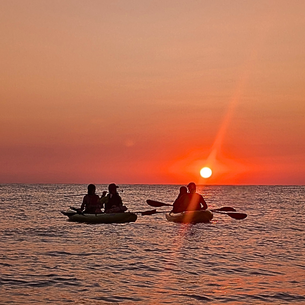 People watching the sunrise from two kayaks on calm morning water.