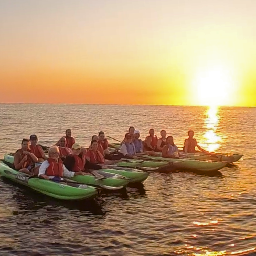 Group of people sitting in kayaks at sunset in Malta on calm water.