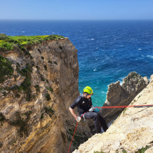 Boy abseiling down a rock face in Xaqqa Valley, Malta, secured with rope and helmet.