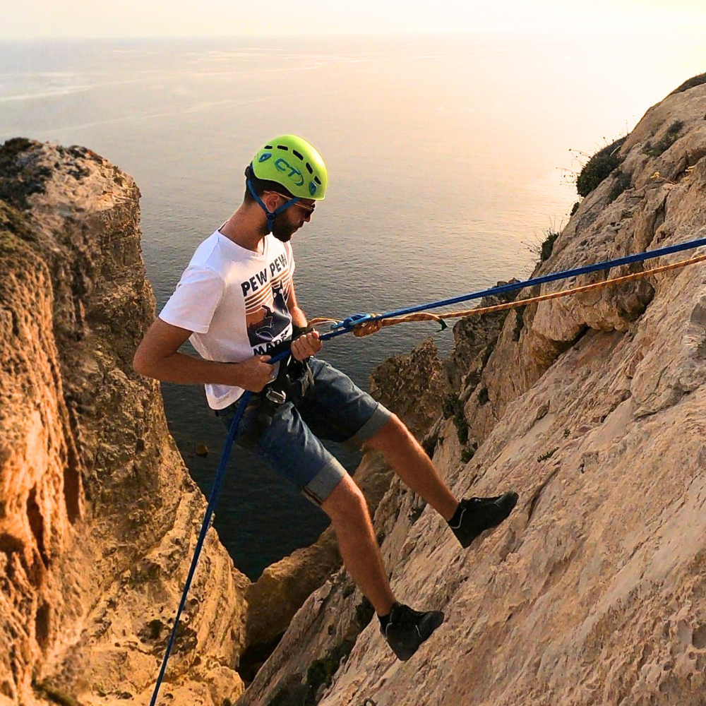 Man abseiling down a rock face in Xaqqa Valley, secured with rope and harness.