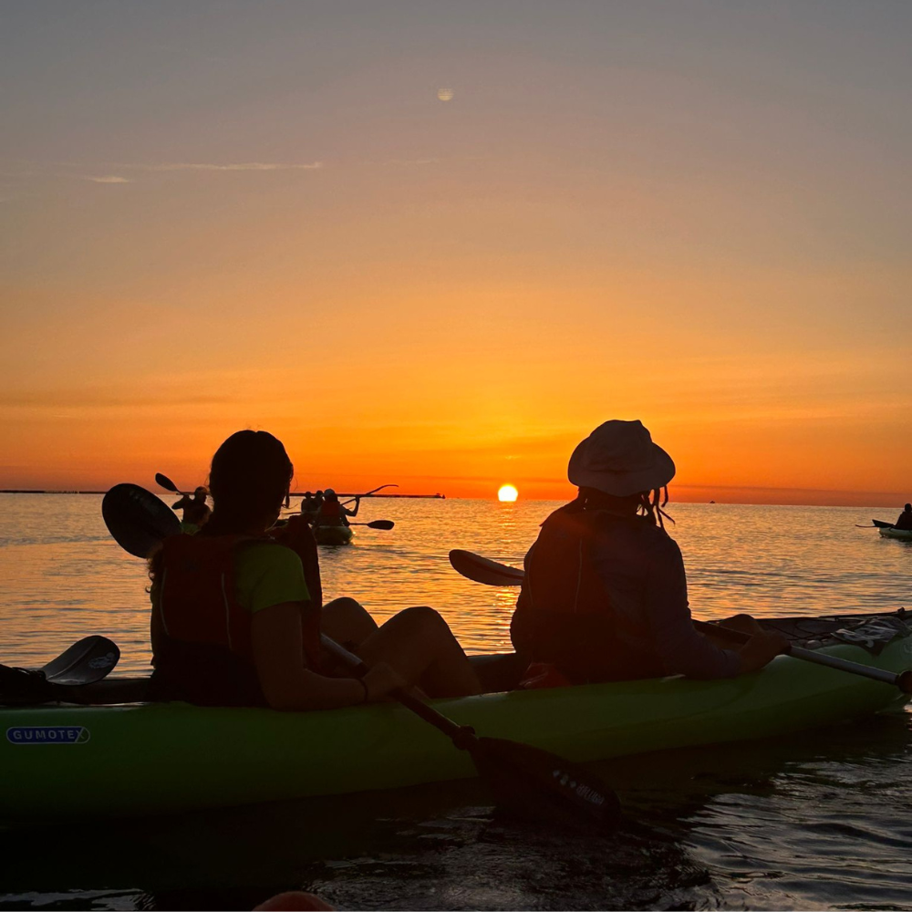 Two people sitting in a kayak watching the sunrise in Malta on calm water.