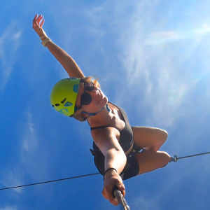 Girl riding a zipline upside down, hanging securely with harness and trolley.