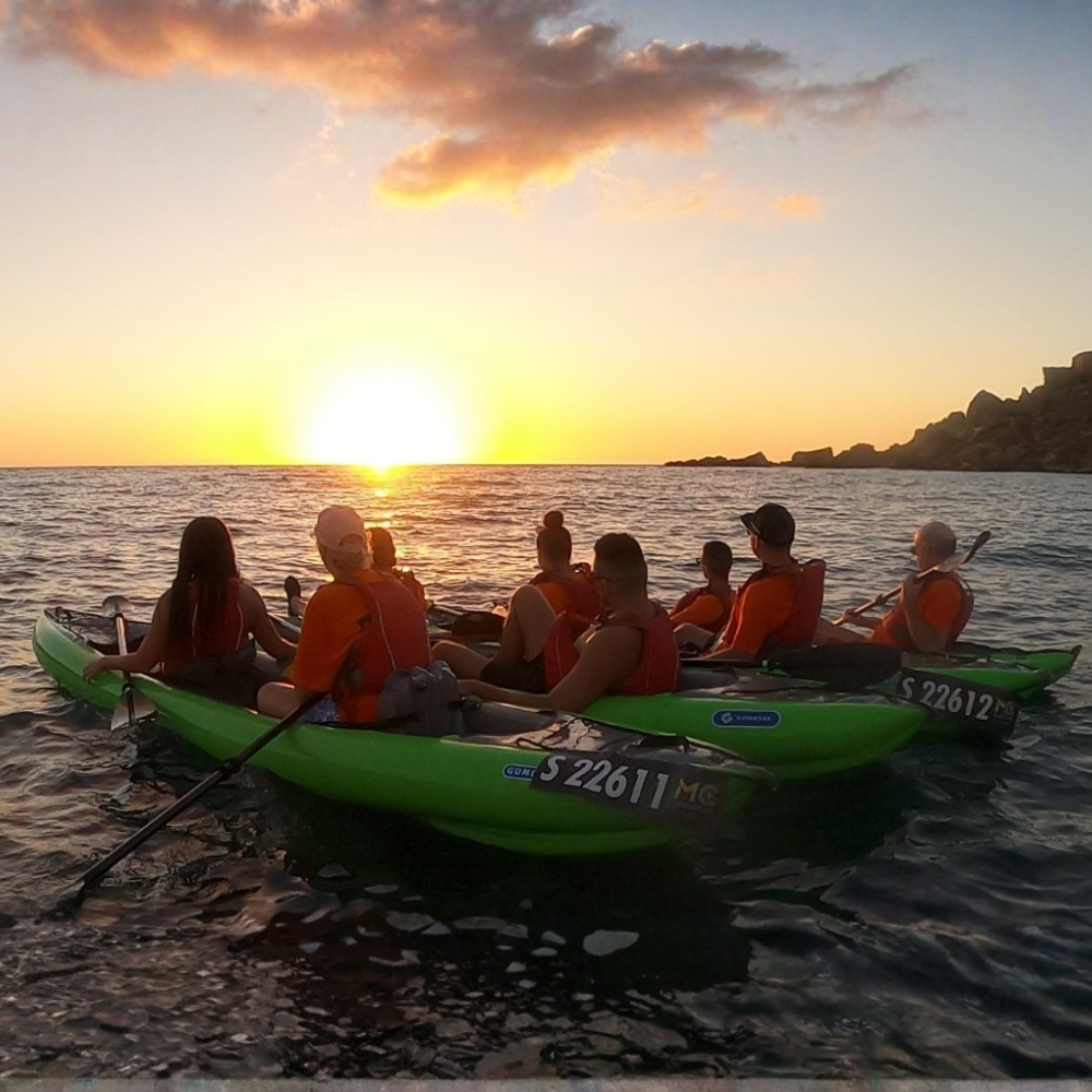 Kayaking group watching the sunset from their kayaks on calm water.